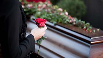 Woman holds rose beside coffin
